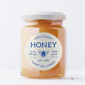 May include: A glass jar of red clover honey with a white label that says "• RED CLOVER. HONEY 8 oz 225 gm 100% pure est. 1989 HAPPY HILL APIARY".
