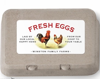 May include: A gray cardboard egg carton with a rectangular label. The label reads "FRESH EGGS" in red, with illustrations of a rooster and hen. Text on the label includes "LAID BY OUR LOCAL HAPPY HENS" and "FROM OUR COOP TO YOUR TABLE."
