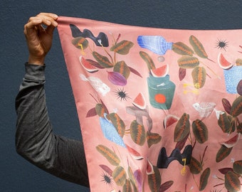 May include: A pink silk scarf with a colorful pattern of leaves, fish, keys, and fruit. The pattern is repeated throughout the scarf.
