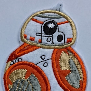 May include: White embroidered patch of a Star Wars character, BB-8, with orange and gold accents. The character is a droid with a round body and a dome-shaped head.