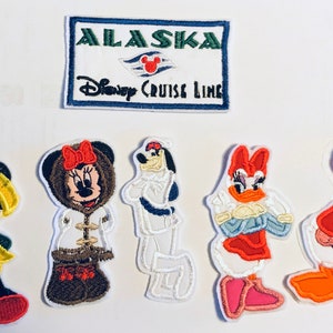 Peut inclure: Cinq patchs brodés thermocollants représentant des personnages Disney. Les patchs comprennent Mickey Mouse portant un imperméable jaune, Minnie Mouse portant un manteau d'hiver marron, Dingo portant une tenue de marin, Daisy Duck portant une robe rouge et Donald Duck portant un gilet bleu. Les patchs sont tous sur un fond blanc. Il y a aussi un patch blanc avec une bordure bleue qui dit "ALASKA Disney Cruise Line" avec un logo rouge de la tête de Mickey Mouse.