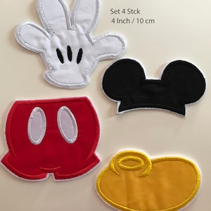 Op de afbeelding: Set van vier 10 cm grote, strijkbare viltpatches met Mickey Mouse: een witte handschoen, zwarte oren, een rode broek en een gele cirkel.