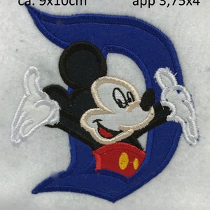 May include: Blue embroidered patch featuring Mickey Mouse in a red shirt with yellow buttons, against a blue background shaped like the letter D. The patch measures approximately 3.75 inches by 4 inches.