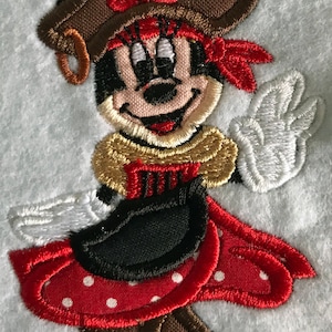 May include: Embroidered patch of a cartoon mouse wearing a brown pirate hat with a red bow, a red bandana, and a red and white polka dot dress.