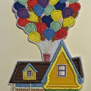 Può includere: Un toppa ricamente ricamata di una casa con tetto marrone e pareti gialle, sollevata da un gruppo di palloncini multicolori.