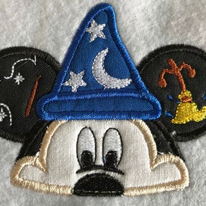 May include: Embroidered patch of Mickey Mouse wearing a blue wizard hat with white stars and a crescent moon. The ears are black with embroidered details.