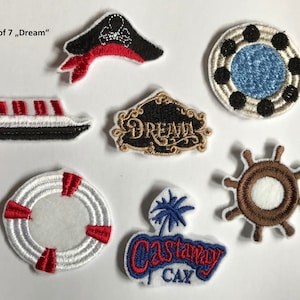 Op de afbeelding: Set van zeven geborduurde strijk-op patches met een piratenhoed, een schip, een reddingsboei, een stuurwiel, een cirkel met een blauw centrum, een bord met de tekst "Dream" en een bord met de tekst "Castaway Cay".