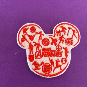 May include: Red embroidered patch in the shape of a Mickey Mouse head with the word "Avengers" and silhouettes of the Avengers characters.