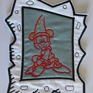May include: A red and gold embroidered patch of Mickey Mouse wearing a wizard hat. The patch is framed in a black and white cartoon style border. The patch is approximately 16cm by 21.5cm.