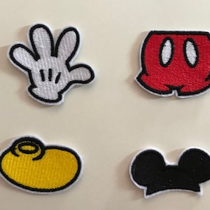Può includere: Quattro toppe ricamate con elementi di personaggi dei cartoni animati. Include un guanto bianco con contorni neri, pantaloncini rossi con dettagli bianchi, una scarpa gialla con un vortice nero e orecchie nere con contorno bianco.