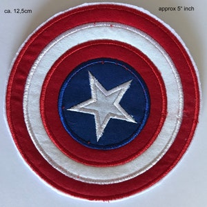 Peut inclure: Un écusson rond brodé, d'environ 12,5 cm de diamètre, représentant un bouclier. Le motif présente des cercles concentriques rouges, blancs et bleus, avec une étoile blanche sur un centre bleu. Idéal pour la décoration.