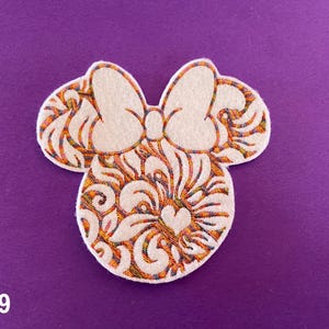 May include: White felt applique of a cartoon mouse head with a bow. The mouse head has a detailed design of orange, yellow, and red swirls and a small heart in the centre.