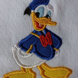 May include: Embroidered patch featuring a cartoon duck wearing a blue sailor hat and a red bow tie. The duck has a yellow beak and white feathers.