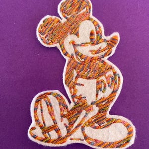 Könnte beinhalten: Ein bunter gestickter Aufnäher von Mickey Mouse, der lächelnd steht. Der Aufnäher ist aus weißem Filz mit bunter Stickerei.