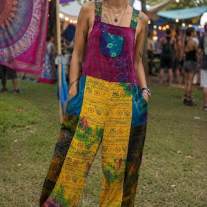 May include: A sleeveless jumpsuit featuring a magenta bodice with a tie-dye chest pocket, paired with yellow and black patterned trousers. The garment has wide shoulder straps, side pockets, and a loose, relaxed fit with gathered ankle cuffs.