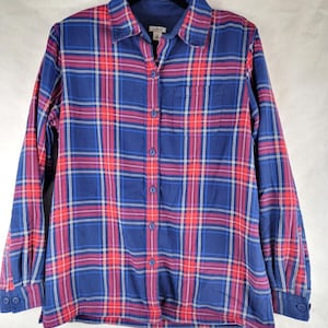 May include: A long-sleeve button-down shirt featuring a plaid pattern in shades of navy blue, bright red, and thin white lines. The shirt includes a pointed collar, a single chest pocket on the left side, and matching blue buttons down the front.