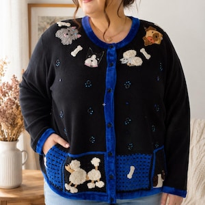 May include: A black button-down cardigan featuring a vibrant blue velvet trim along the neckline and front placket. The garment is decorated with embroidered dog appliques, white bone motifs, and small blue bead accents, with two front pockets.