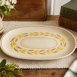 May include: An oval ceramic serving platter with a cream-colored base and a central decorative border featuring a repeating pattern of yellow and brown tulip-like floral motifs, finished with a thin brown line along the outer rim edge.