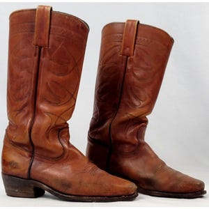 May include: A pair of brown leather cowboy boots. The boots have a classic design with decorative stitching and a pointed toe. The boots have a heel and a pull strap at the top. The boots are approximately 12 inches tall.