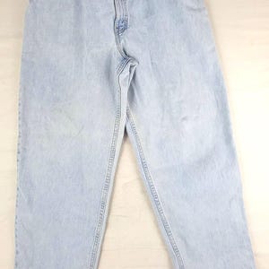 May include: Light blue denim jeans with a relaxed fit. The jeans have a classic five-pocket design, a button and zipper closure, and belt loops. The brand name "Staggy" is visible on the waistband. The jeans are made of a light-wash denim.