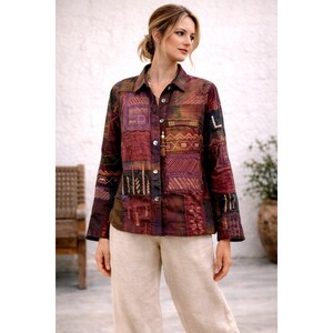 May include: A long-sleeved button-down shirt featuring a patchwork design in shades of deep red, purple, and brown. The garment displays various geometric patterns, including stripes, zigzags, and squares, with visible stitching details throughout.