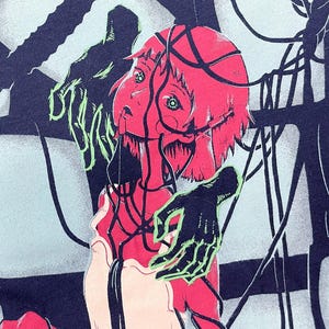 May include: Dark blue t-shirt featuring a surreal illustration. A red-haired figure with green eyes is entangled in black wires, with a green-outlined hand reaching out. The text "APRIL LAPIN" is in green on the left side.