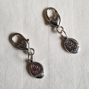 May include: Two silver charm clips with heart-shaped clasps. The charms are oval-shaped with the words "Love much" and "Laugh often" engraved on them.