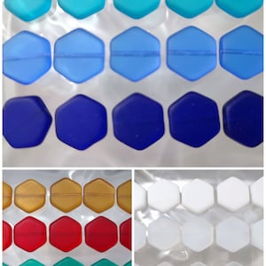 Peut inclure: Assortiment de perles de verre hexagonales de différentes couleurs, notamment turquoise, bleu, bleu foncé, or, rouge et vert. Les perles sont disposées en rangées, chaque rangée présentant une couleur différente.
