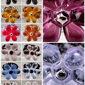 May include: A collage of ten flower-shaped rings. The rings are made of different materials, including glass, plastic, and metal. The rings are all in different colors, including black, red, blue, yellow, and purple.
