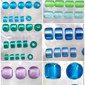 Peut inclure: Assortiment de perles de verre colorées de différentes formes et tailles. Les perles sont disposées en rangées sur une surface blanche. Les perles sont translucides et ont une finition brillante.