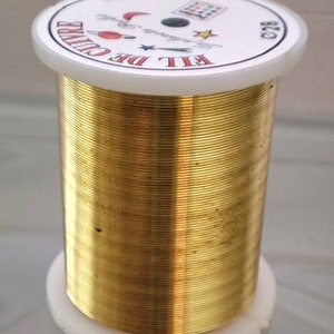 Könnte beinhalten: Eine Spule mit goldfarbenem Draht und einem weißen Etikett mit der Aufschrift "FIL DE CUIVRE 22 METRES 0.20".