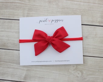 Puede incluir: Diadema de tela roja con lazo sobre un fondo blanco. La diadema está hecha de un material suave y elástico, perfecto para bebés y niños pequeños. El lazo está atado con un simple nudo y tiene aproximadamente 5 cm de ancho. La diadema es una excelente manera de agregar un toque de estilo a cualquier atuendo.