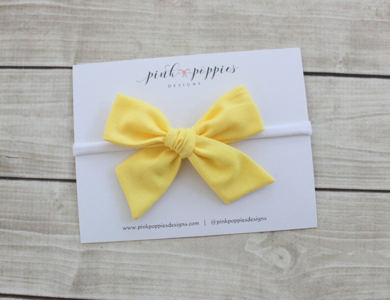 May include: A yellow fabric bow headband on a white background. The headband is made of a soft, stretchy material and is perfect for babies and toddlers.
