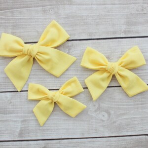 May include: Three yellow fabric hair bows of different sizes. The bows are tied in a knot in the center and have a soft, fluffy texture.