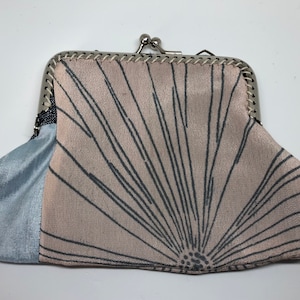 May include: A small, pink and blue fabric purse with a silver clasp. The purse has a black and white sunburst design on the front.