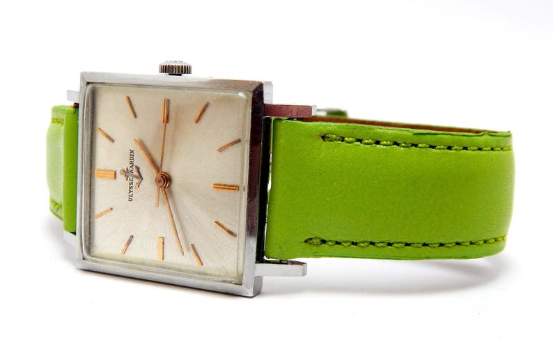 Pu&ograve; includere: Un orologio da polso vintage Ulysse Nardin con cassa quadrata color argento e quadrante chiaro con lancette e indici dorati. L'orologio ha un cinturino in pelle verde brillante. Il quadrante mostra il marchio Ulysse Nardin.