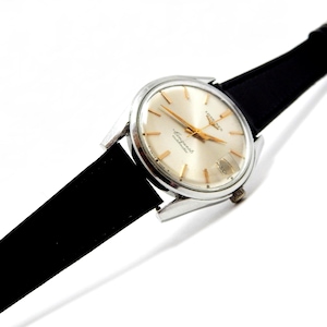 Puede incluir: Un reloj de pulsera vintage con caja plateada, esfera clara y agujas e indicadores dorados. El reloj tiene una correa de cuero negro. La esfera del reloj muestra el texto "Longines Conquest Automatic".
