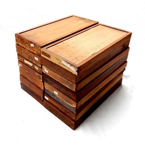 May include: A collection of vintage wooden boxes, stacked together. The boxes are various shades of brown, showing signs of age and use. Some boxes have labels and handwritten notes. The boxes are stacked on top of each other.