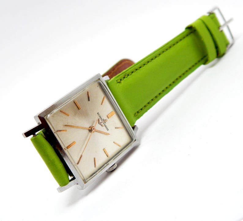 Pu&ograve; includere: Un orologio da polso quadrato vintage con cassa argentata e cinturino in pelle verde chiaro. Il quadrante dell'orologio &egrave; di colore champagne chiaro con lancette e indici dorati. Il cinturino &egrave; largo circa 2 cm.