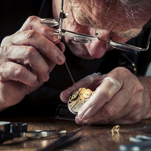 May include: A close-up of a watchmaker at work, meticulously repairing a watch. The watchmaker is wearing a loupe and using small tools to work on the watch's intricate internal mechanisms. The watch parts are gold and silver.