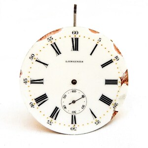 Peut inclure: Cadran d'horloge blanc avec des chiffres romains noirs pour les heures et des marques noires pour les minutes. Le cadran porte l'inscription "LONGINES" en noir en haut. Le cadran est l&eacute;g&egrave;rement endommag&eacute;.