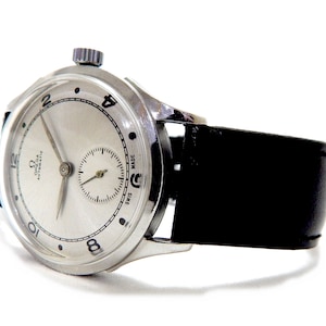 Könnte beinhalten: Eine Vintage Omega Automatic Armbanduhr in Silber mit einem schwarzen Lederarmband. Das Zifferblatt der Uhr ist silberfarben mit schwarzen Ziffern und Zeigern. Sie hat eine kleine Sekundenscheibe und eine strukturierte Krone. Weißer Hintergrund.