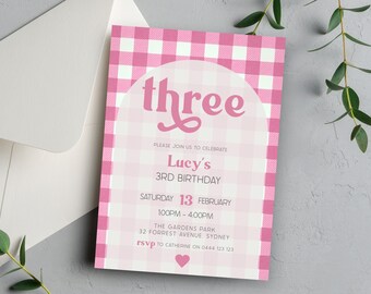 Pode incluir: Convite com padrão xadrez rosa e branco com um arco rosa e o texto "three" em uma fonte retrô rosa. O convite é para o 3º aniversário de Lucy, no sábado, 13 de fevereiro, das 13h às 16h no The Gardens Park, 32 Forrest Avenue, Sydney. RSVP para Catherine no 0444 123 123.