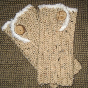 Puede incluir: Un par de guantes sin dedos de punto beige con ribete blanco y botones de madera marrón.