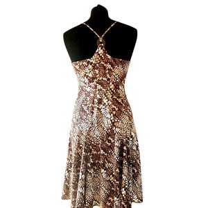 Peut inclure: Une robe sans manches arrivant au genou avec un motif abstrait marron et blanc composé de formes répétitives évoquant des feuilles. Le vêtement présente un dos nageur avec de fines bretelles reliées par un anneau central, un corsage ajusté et une jupe évasée.