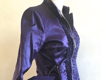May include: A purple satin jacket with a ruffled front and zipper closure. The jacket has a stand-up collar and long sleeves.