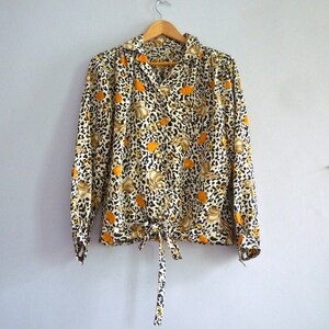 May include: A long-sleeved blouse with a leopard print and orange floral pattern. The blouse has a tie at the waist and a button-up front.