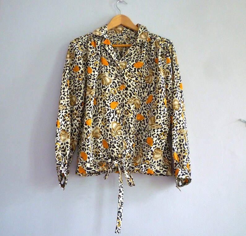 May include: A long-sleeved blouse with a leopard print and orange floral pattern. The blouse has a tie at the waist and a button-up front.