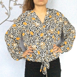 May include: A white blouse with a leopard print and orange floral accents. The blouse has a V-neck and long sleeves with a tie at the waist.
