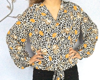 May include: A white blouse with a leopard print and orange floral accents. The blouse has a V-neck and long sleeves with a tie at the waist.